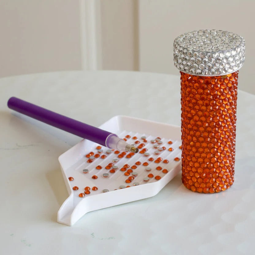 A pill bottle covered with with rhinestones beside a tray and a pen.